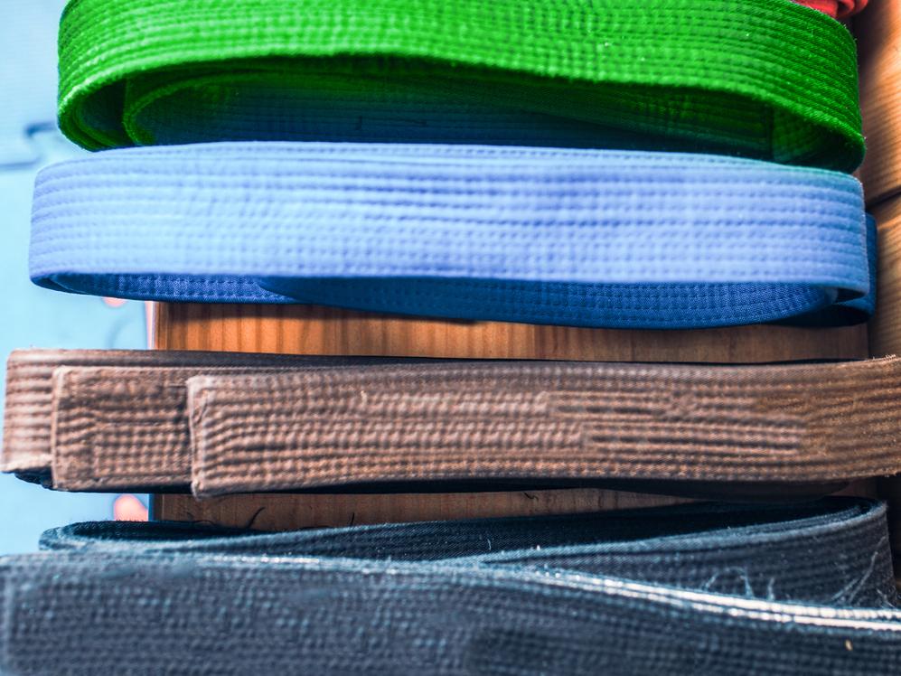 Bunte, aufgerollte Gürtel in verschiedenen Farben liegen übereinander auf einem Holztisch.
